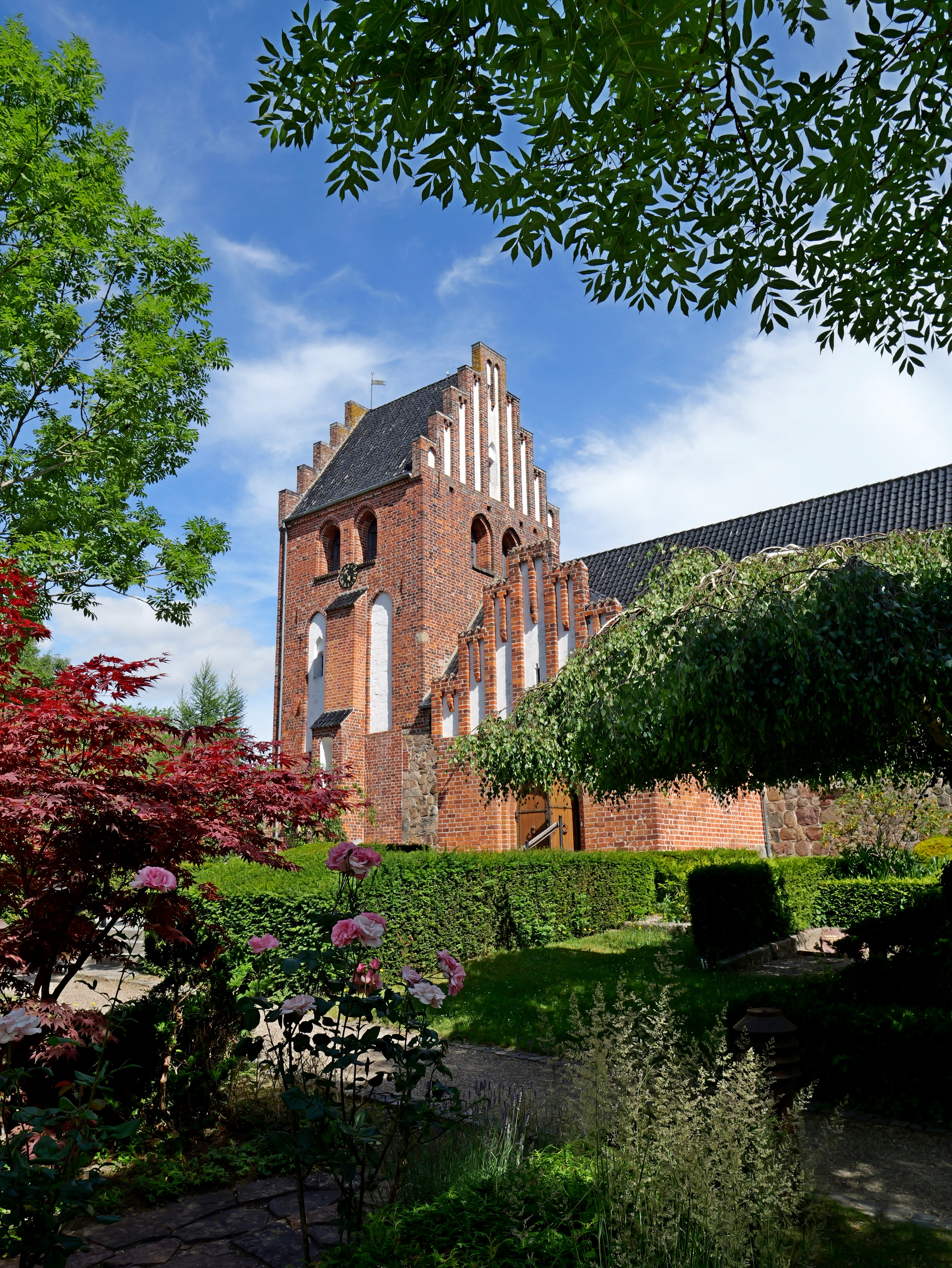 Birkerød Kirke taget fra kirkegården med træer og blomster